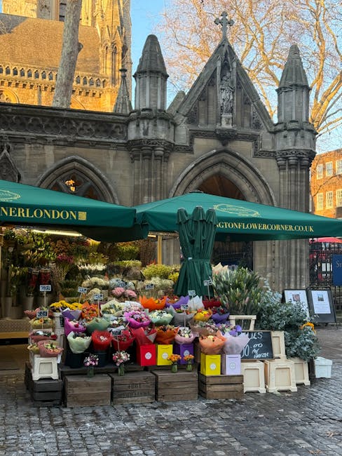 An outdoor flower stand situated in front of a historic stone church with Gothic architectural details, including pointed arches and decorative spires. The stand displays a vibrant assortment of fresh